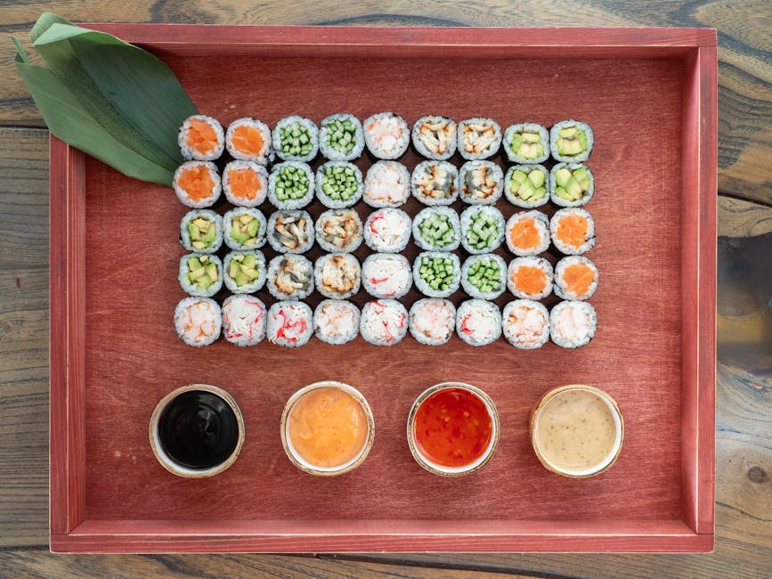 Vibrant sushi assortment with various sauces, artistically presented on a wooden tray.