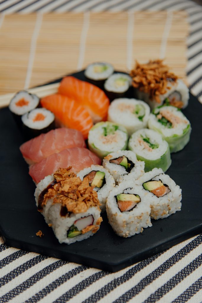 Abundance of traditional Japanese tasty sushi rolls with fresh fish served on black plate on table with tablecloth in light room